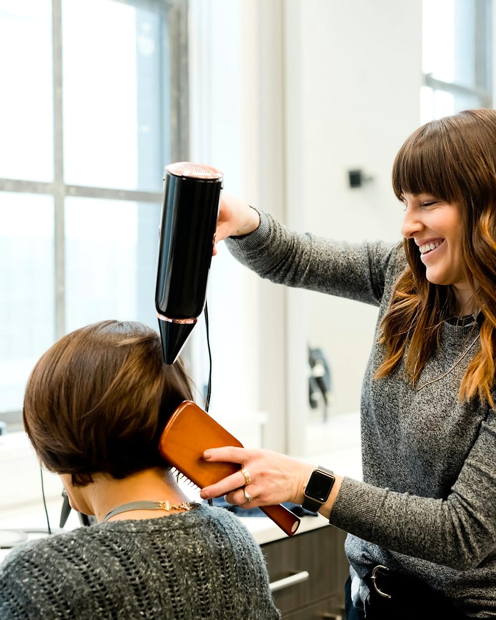 Estilista secando y peinando el cabello de una clienta